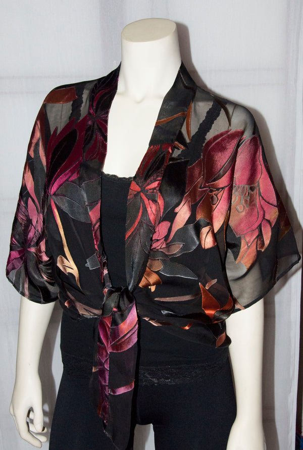 The black and red magnolia devore kimono jacket is a beautiful blouse that can be worn over a black dress . The scarf edges are worn tied at the waist. It can also be worn with the scarf edges untied.